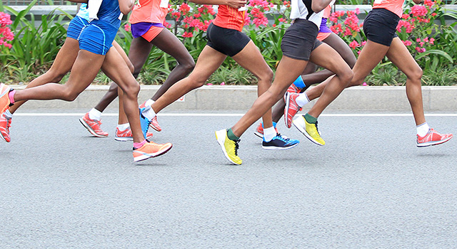 A group of runners participating in a race, captured mid-stride on an urban street with a clear sky background.